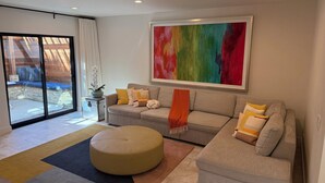 Una sala moderna con un sofá gris, un reposapiés y un cuadro abstracto colorido.