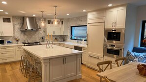 Una cocina moderna con armarios blancos, una isla grande, electrodomésticos de acero inoxidable e iluminación colgante.