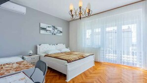 Un dormitorio con cama, mesita de noche, silla y un ventanal con cortinas traslúcidas.