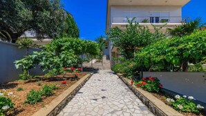 Un sendero conduce a un edificio con balcón, rodeado de jardines y árboles bien cuidados.