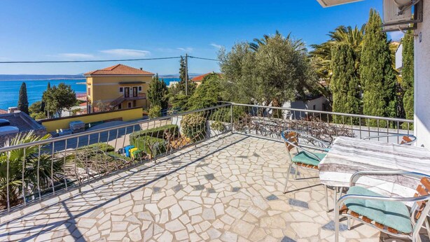Una terraza con suelo de piedra, baranda de metal y mobiliario exterior.