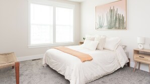 Un dormitorio con una cama grande, un ventilador de techo, una ventana, una mesita de noche y una pintura de un cactus.