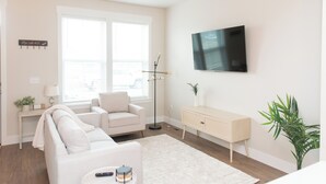 Una sala de estar moderna con un sofá, una mesita, una lámpara de pie, un televisor y una planta.