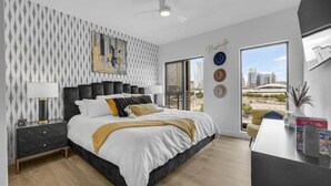 Un dormitorio moderno con una cama grande, una mesita de noche, un escritorio y vistas a la ciudad a través de un amplio ventanal.
