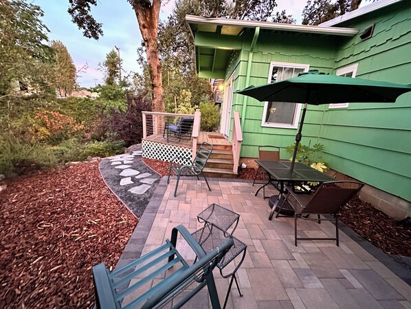 A patio area with a table and chairs, a green umbrella, and a wooden deck leading to a house.