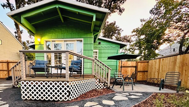 A green house with a porch, outdoor seating, and a stone pathway.