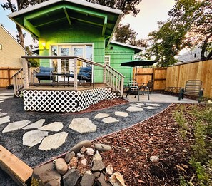 A green house with a porch, outdoor seating, and a stone pathway.
