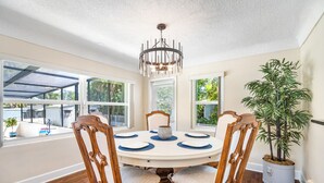 Un comedor con una mesa redonda, cuatro sillas de madera, una araña y una planta en maceta.