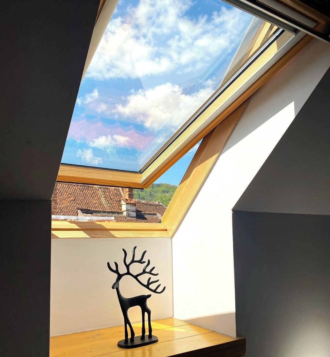 Ein Oberlicht mit Holzrahmen, eine schwarze Hirschskulptur und Blick auf Gebäude und Grünflächen.