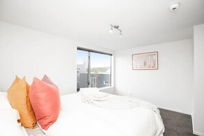 A bedroom with a large bed, a window, and a ceiling light. - Cosy, Central & Convenient (Christchurch)