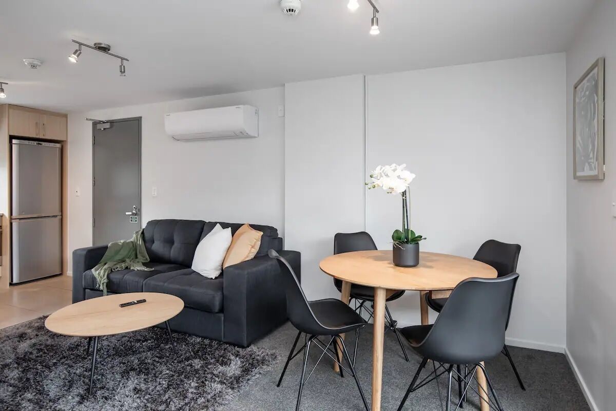Een moderne woonkamer met een zwarte bank, een ronde houten tafel en zwarte stoelen.