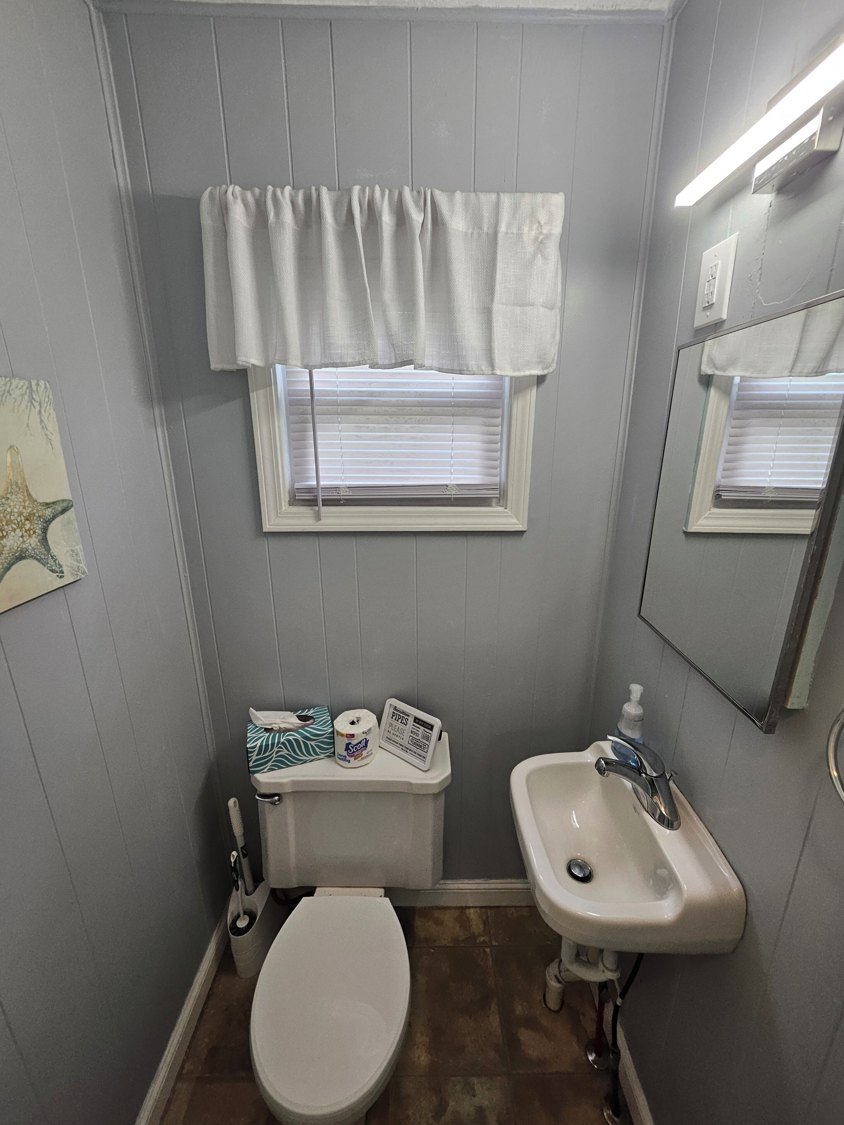 A small bathroom with a toilet, sink, and window with blinds.