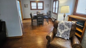 Una sala de estar con un sillón de cuero marrón, una mesa de comedor con sillas y una araña.