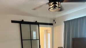 Una camera da letto con un letto, un comodino, una lampada, una ventola a soffitto e una porta scorrevole.