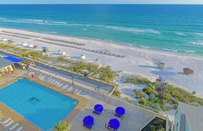 A beach resort with a swimming pool, sun loungers, and a boardwalk leading to the beach.