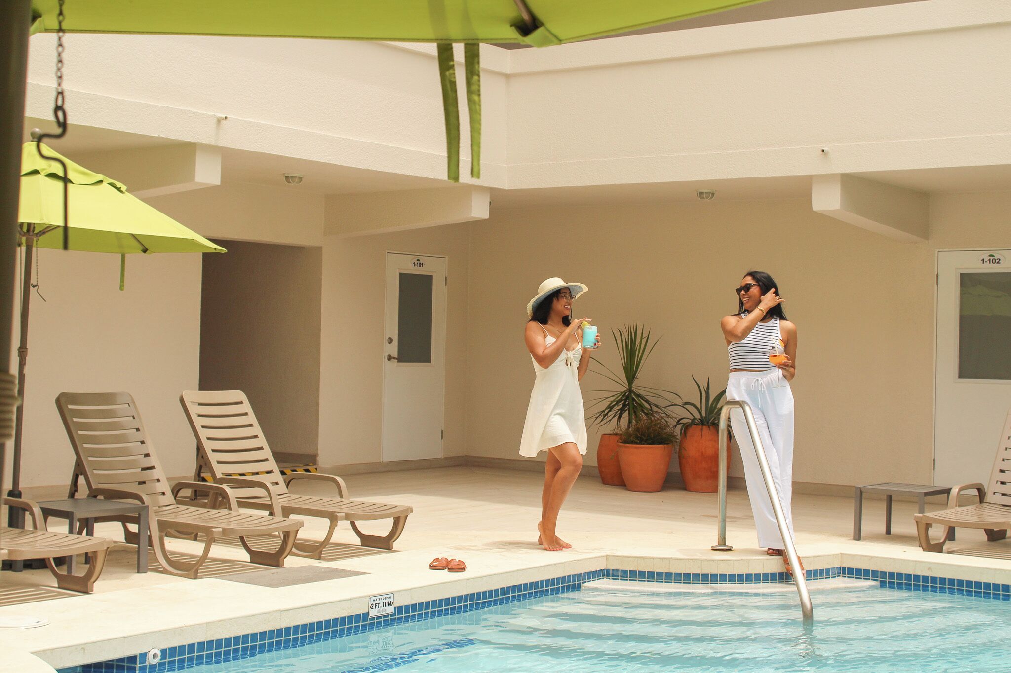 A pool area with lounge chairs, a pool, and potted plants.