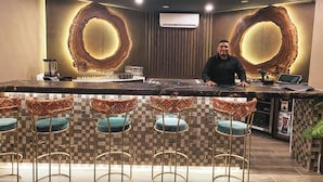A bar area with a central counter, bar stools, and a person standing behind the counter. - Bananas On The Beach (San Pedro)