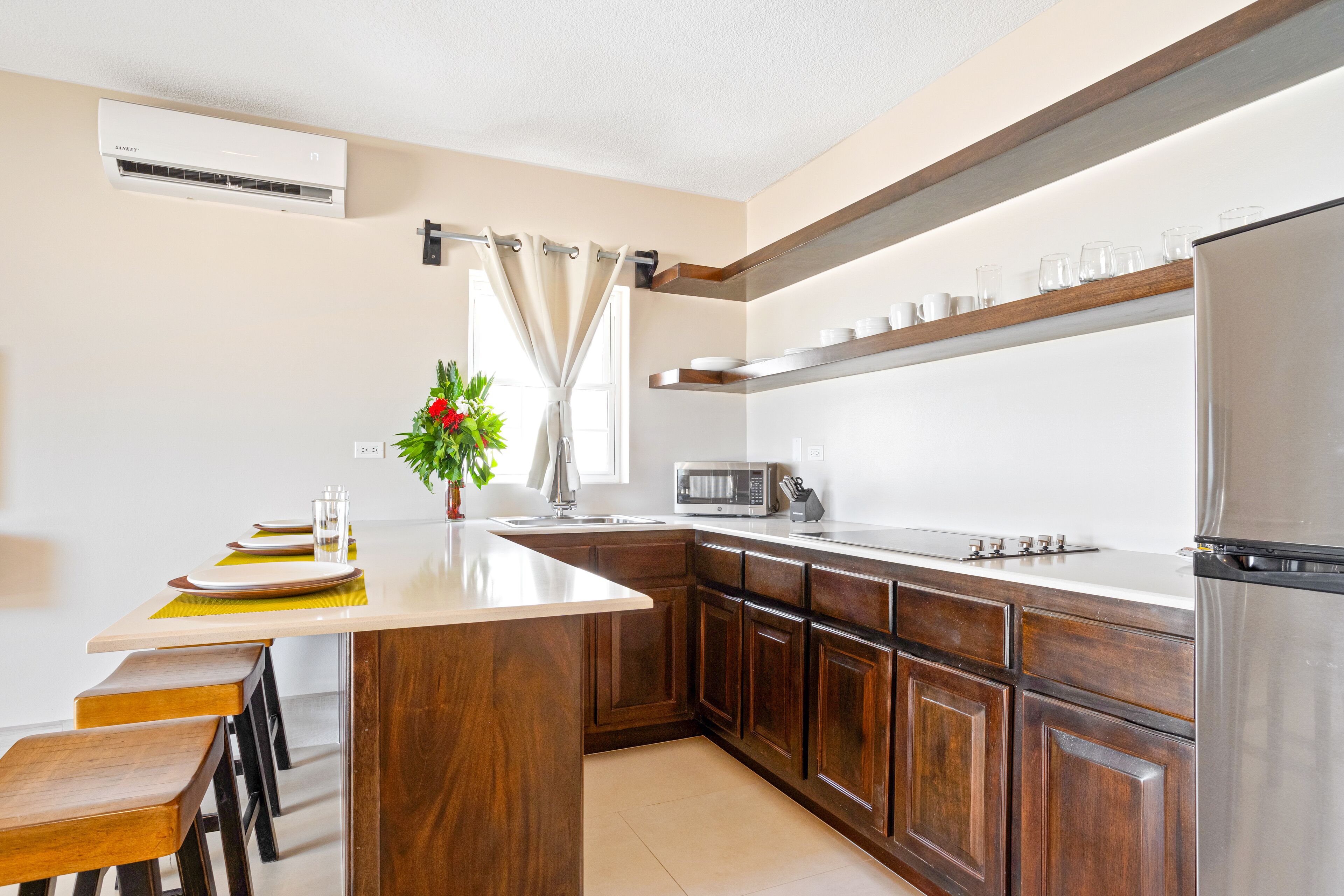 Una cucina moderna con mobili in legno, un frigorifero in acciaio inossidabile, un forno a microonde e un'area pranzo con una pianta.