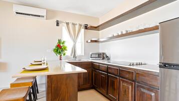 Una cocina moderna con armarios de madera, un refrigerador de acero inoxidable, un microondas y una zona de comedor con una planta.