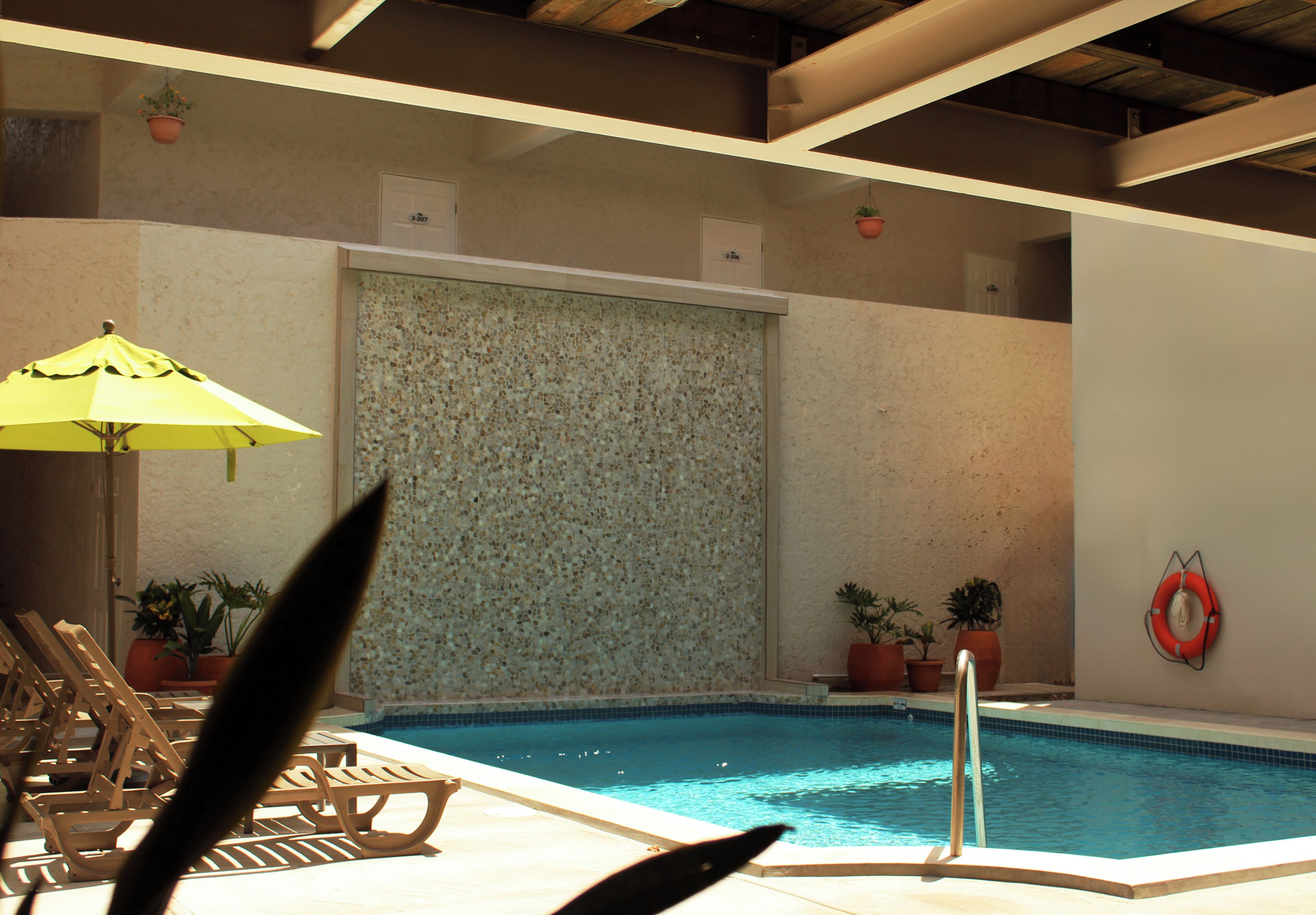 Une piscine intérieure avec un mur carrelé, des plantes en pot, un dispositif de sauvetage et des chaises longues en bois.