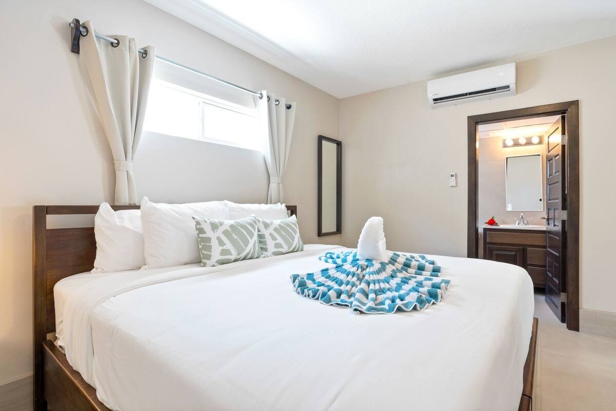 A hotel room with a large bed, a bathroom with a mirror and sink, and a window with curtains.