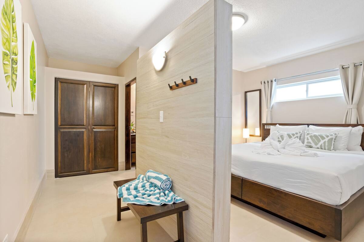 A bedroom with a bed, a wooden bench, a coat rack, and a window with curtains.