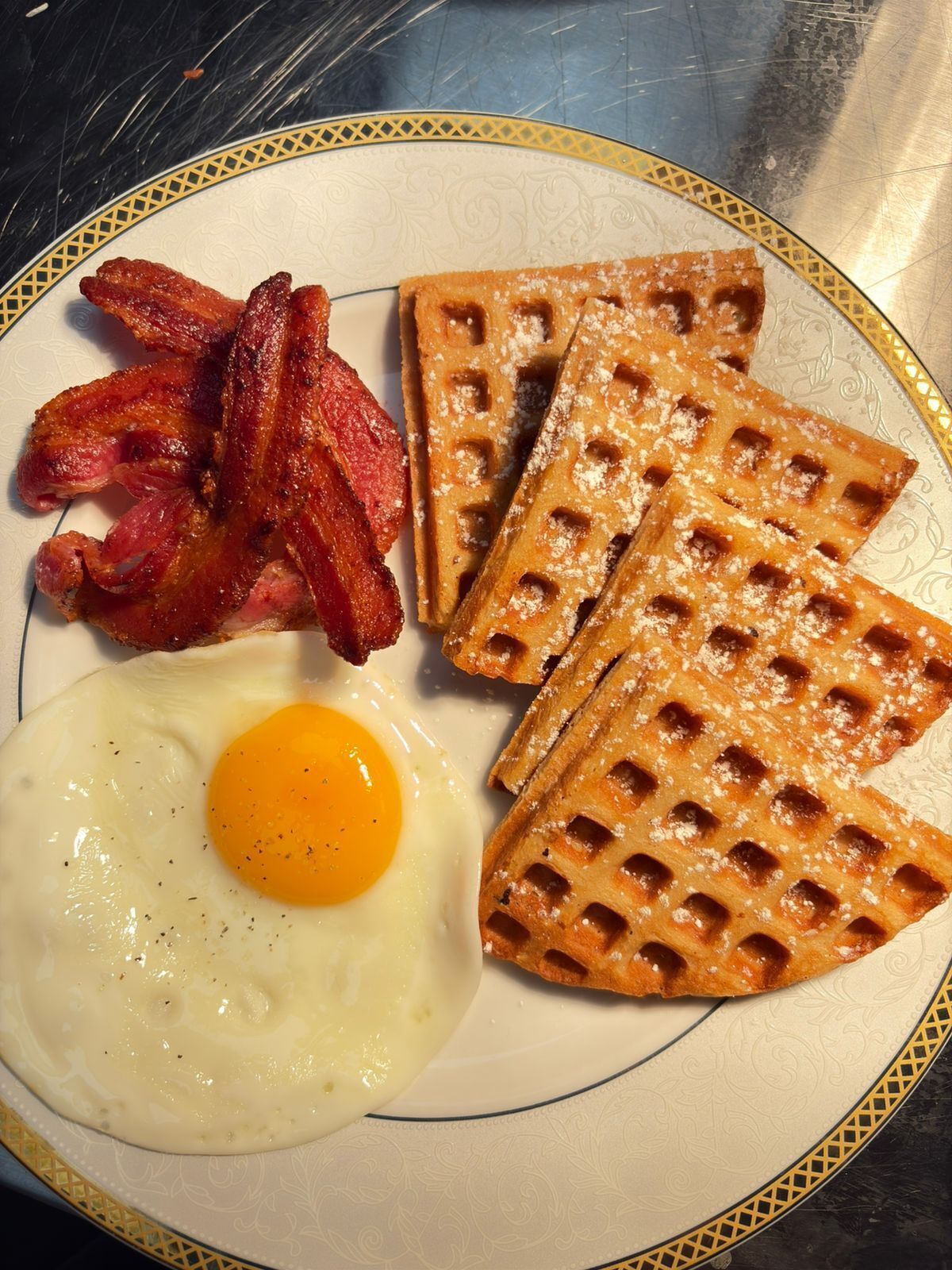 A plate with bacon, waffles, and a fried egg.