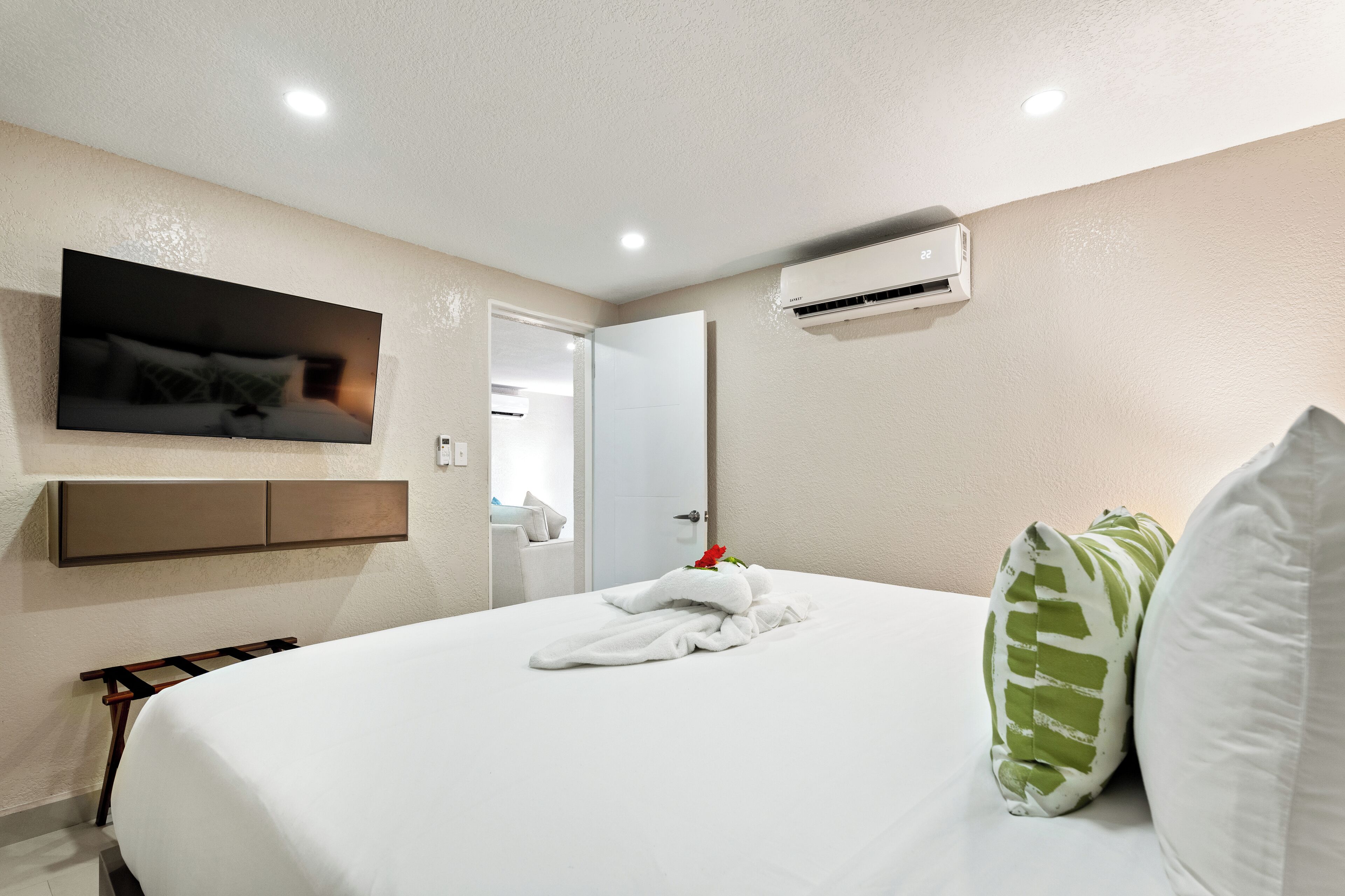 Een hotelkamer met een bed, een wandgemonteerde televisie, een airconditioner en een deur naar een andere kamer.