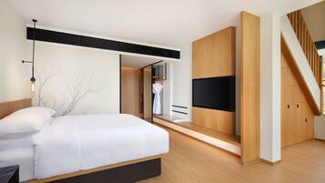 A modern bedroom with a large bed, built-in TV, wooden flooring, and a staircase.