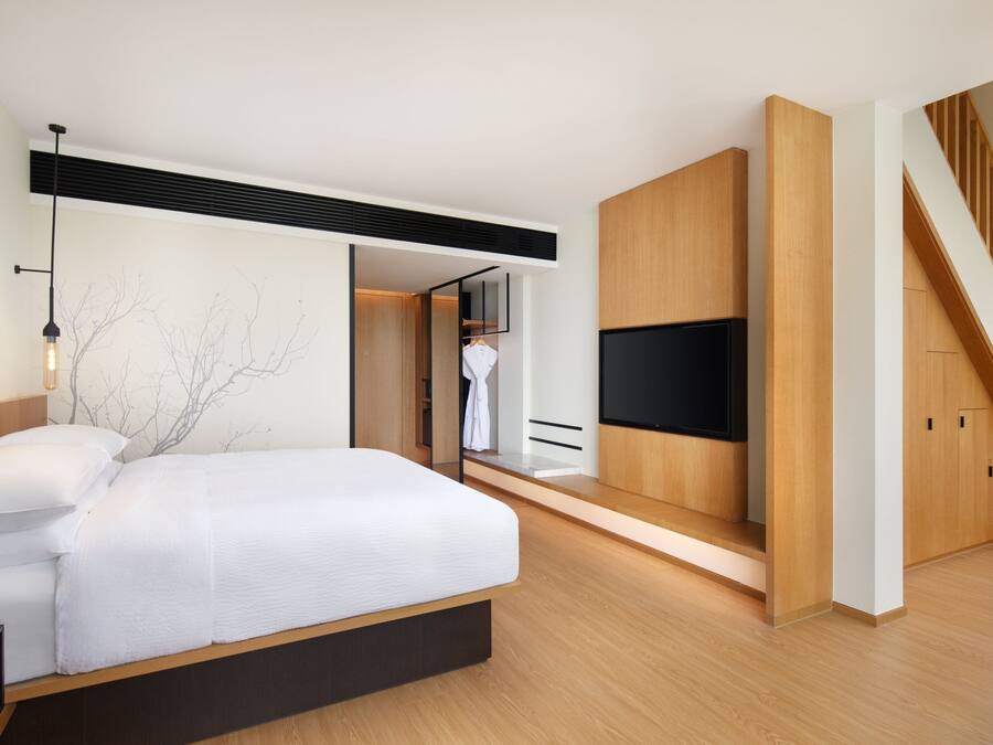 A modern bedroom with a large bed, built-in TV, wooden flooring, and a staircase.