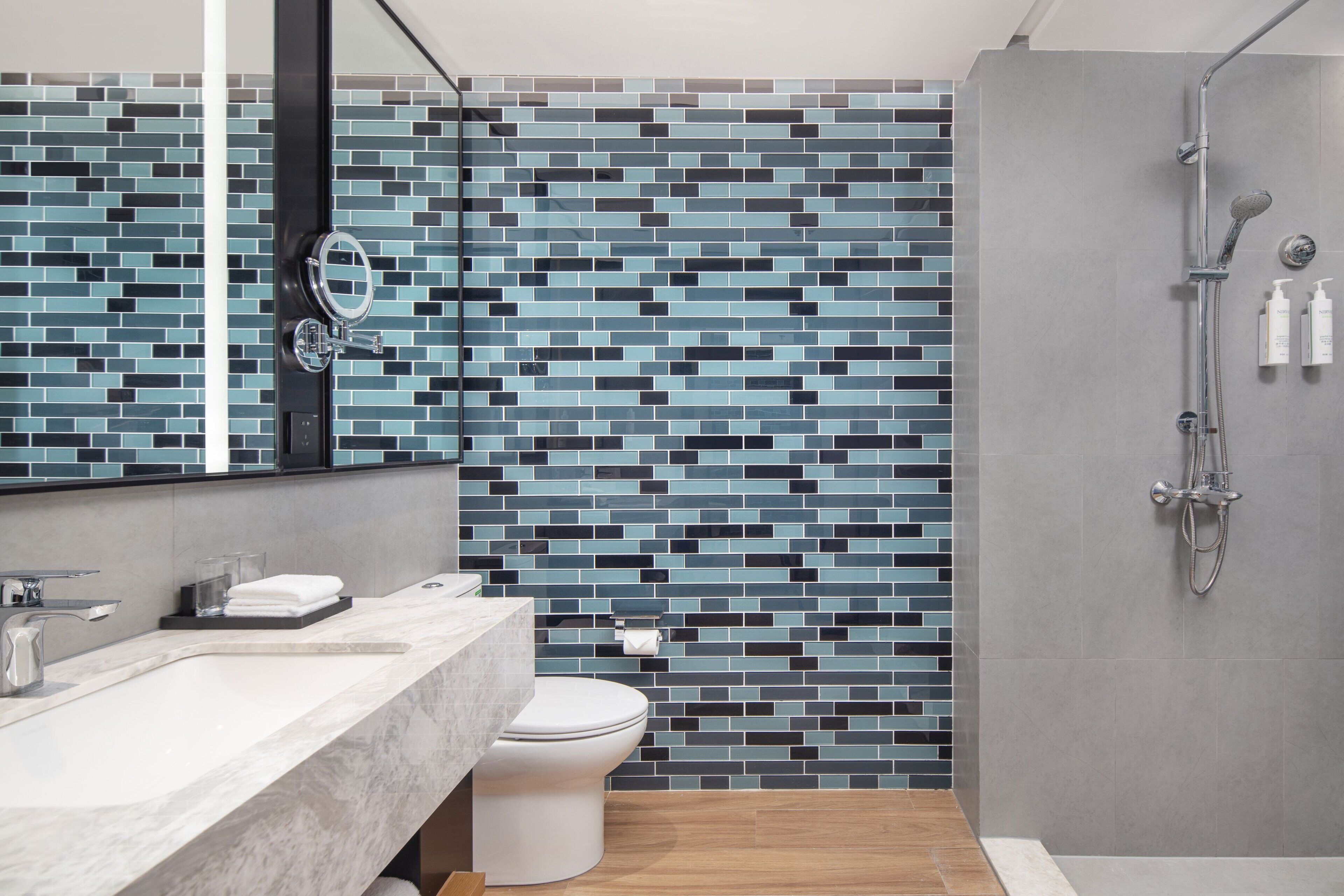 A modern bathroom with a tiled backsplash, a toilet, a sink with a mirror, and a shower area.