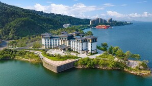 Un hotel frente al agua con varias construcciones, un puente y vistas al mar y montañas distantes.