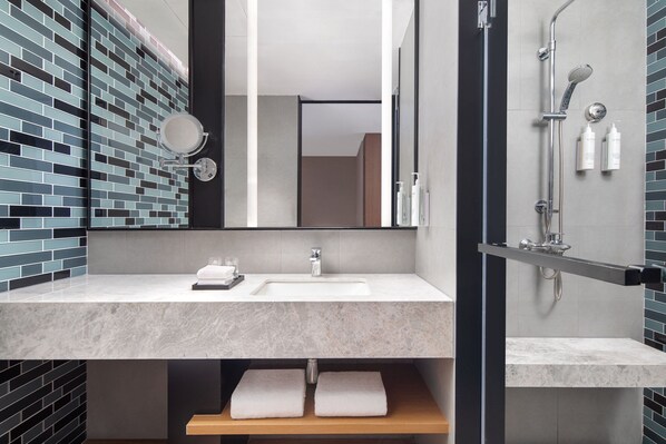 Un baño moderno con un lavamanos de mármol, un espejo grande y una zona de ducha.