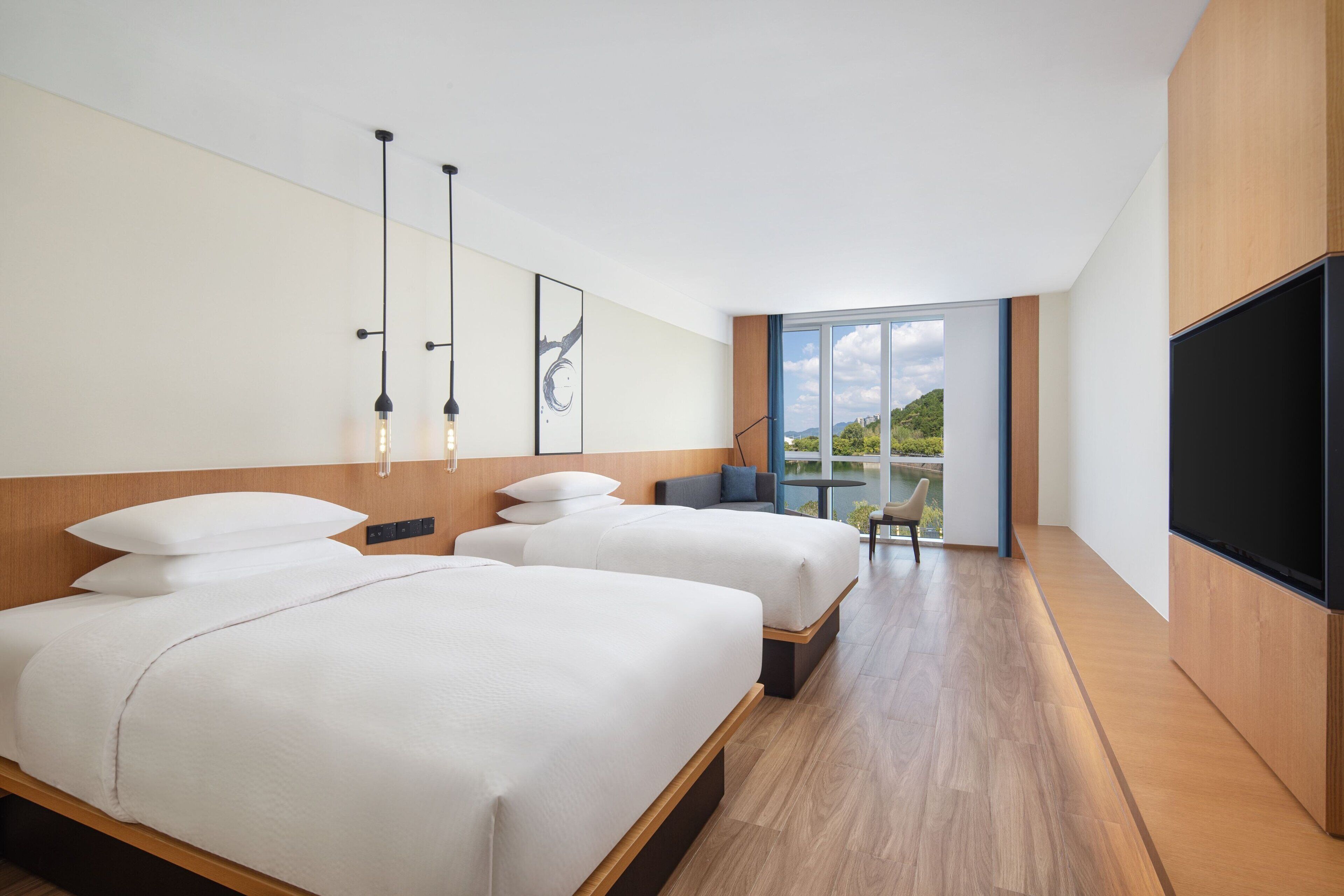 A modern hotel room with two beds, a large TV, and a balcony with a view.