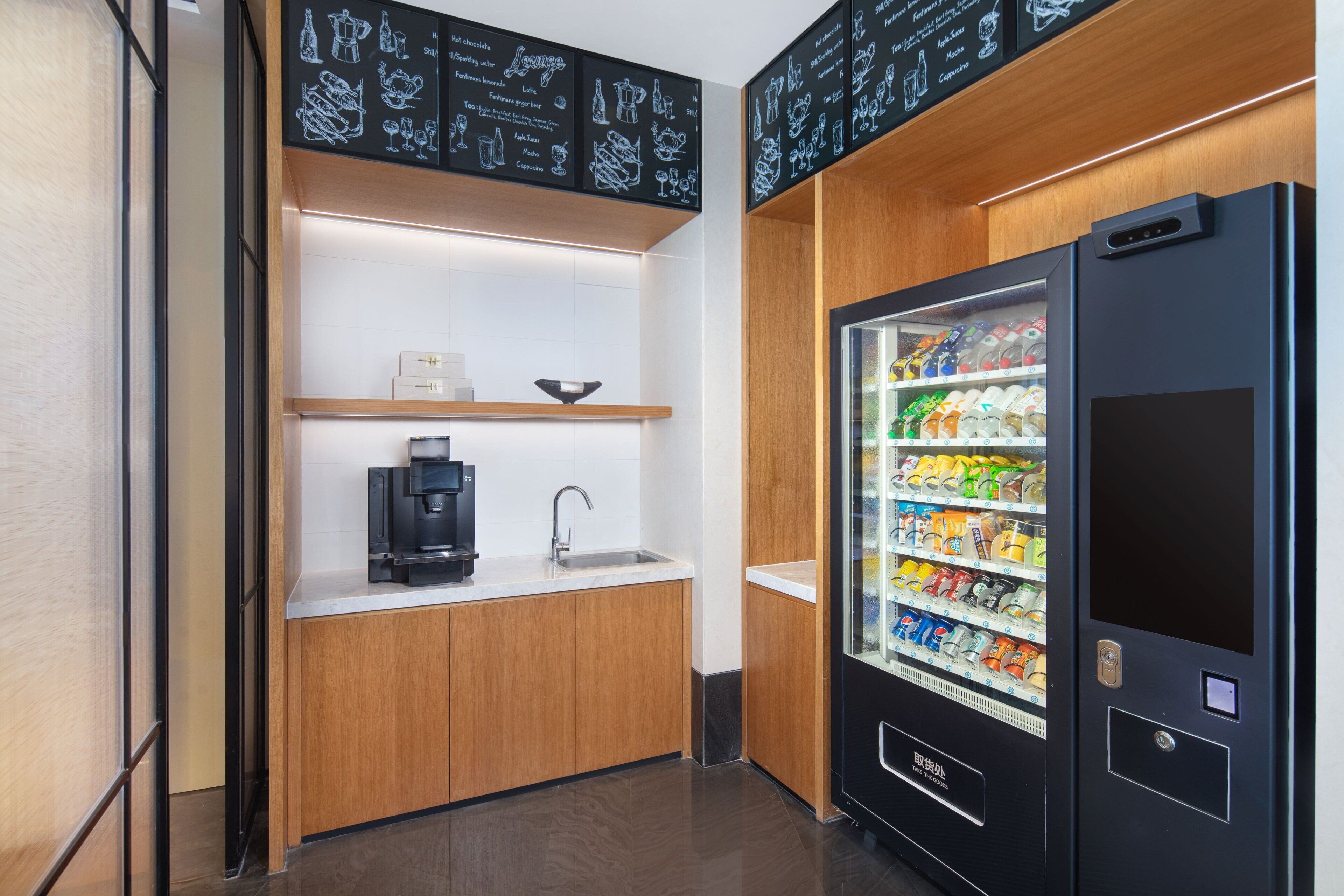 Una kitchenette compacta con cafetera, un lavamanos y una máquina expendedora de bebidas.