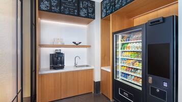 Una kitchenette compacta con cafetera, un lavamanos y una máquina expendedora de bebidas.