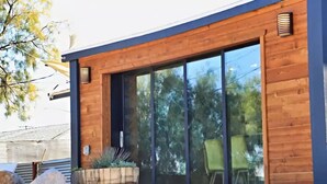 Un edificio moderno con pareti esterne in legno, ampie porte scorrevoli in vetro e posti a sedere all'aperto.