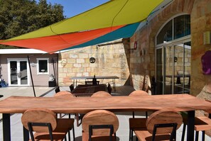 Patio esterno con tavolo e sedie di legno, un muro in pietra e un gazebo colorato.