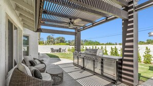 An outdoor patio with wicker furniture, a grill, and a pergola structure.
