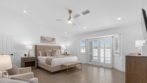 A spacious bedroom with a large bed, a ceiling fan, and a sliding glass door leading to a balcony.