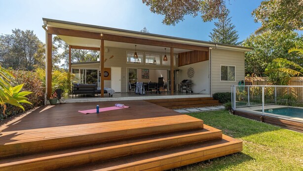 Una casa moderna con un porche cubierto, piscina y un jardín cuidado.