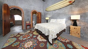 Une chambre à coucher avec un lit, deux tables de chevet, une planche de surf et un tapis à motifs.