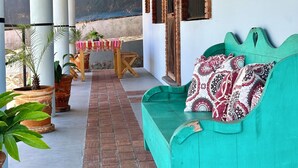 Un espace extérieur aménagé avec un coin salon abrité, comprenant un canapé turquoise, des plantes en pot et une décoration rustique avec notamment un crâne de vache et des arches en briques.