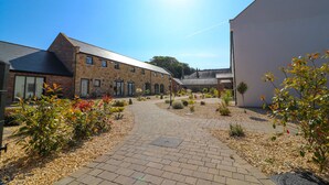 A courtyard with a paved walkway, stone buildings, and various plants. - Northumberland Luxury Stays - The Gavel (Northumberland)