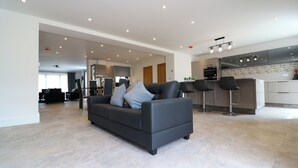 A modern living room with a dark grey sofa, a kitchen area with a built-in island, and a dining area with bar stools. - Northumberland Luxury Stays - The Gavel (Northumberland)