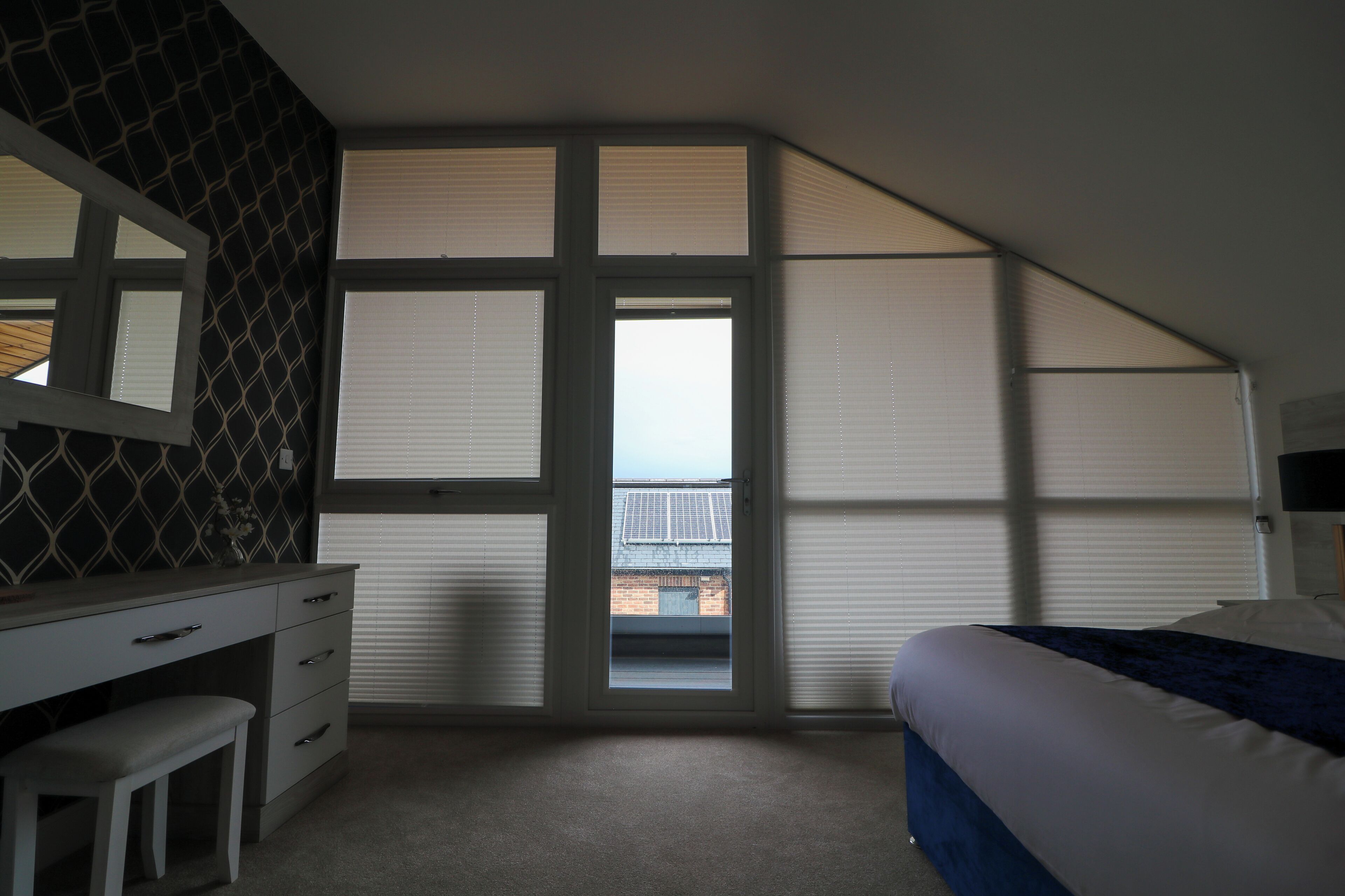 A bedroom with a large window, a desk, and a bed.