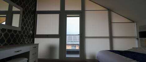 A bedroom with a large window, a desk, and a bed.