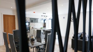 A modern kitchen with a central island, dining area with chairs, and a living room with a sofa. - Northumberland Luxury Stays - The Gavel (Northumberland)