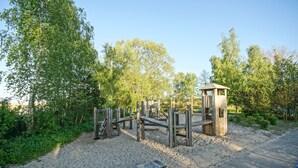 A playground with wooden structures and a small wooden building, surrounded by trees and a paved path. - Apartment 'Am Stettiner Haff' with Private Pool, Private Terrace and Wi-Fi (Mönkebude)