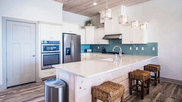 Una cocina moderna con armarios blancos, una isla grande con taburetes, electrodomésticos de acero inoxidable y un salpicadero color turquesa.